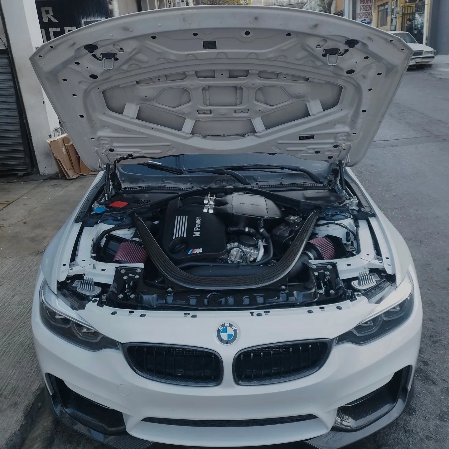 BMW blanco con el cofre abierto y el motor a la vista